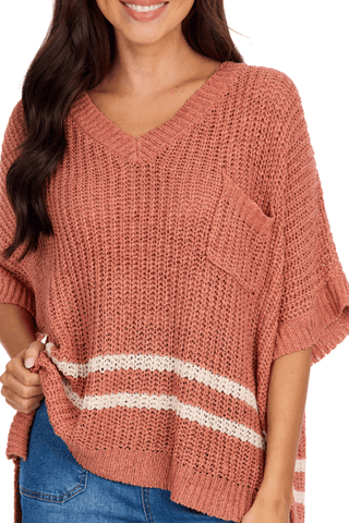 Woman wearing a pink knit sweater with a V-neck and short sleeves, paired with blue jeans.