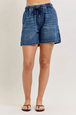 Blue denim shorts worn by a person on a plain background