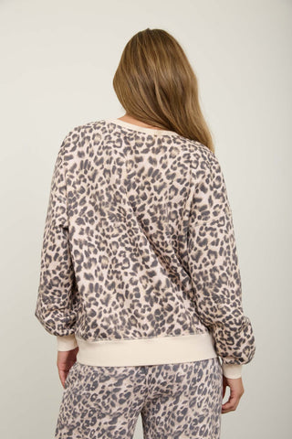 A woman viewed from behind wearing a beige and gray leopard print sweatshirt with cream ribbed trim, paired with matching leopard print pants, against a plain light gray studio background.