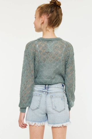 Person wearing a green knitted sweater and denim shorts on a white background