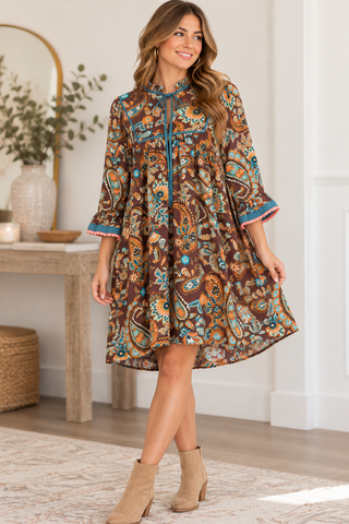 A woman models a brown paisley dress with blue and orange accents in a bright, modern room setting.