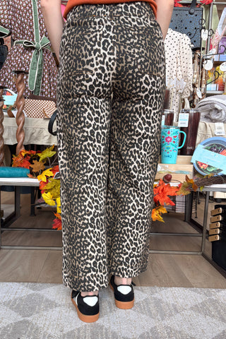 A person shown from the back wearing leopard-print wide-leg pants, an orange top, and black Mary Jane shoes in a retail store setting.