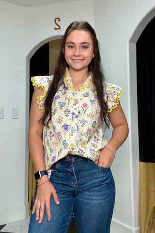 Woman wearing a floral blouse and blue jeans indoors.