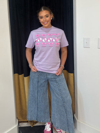 Person wearing a light purple t-shirt with text and blue jeans standing in front of a black curtain.