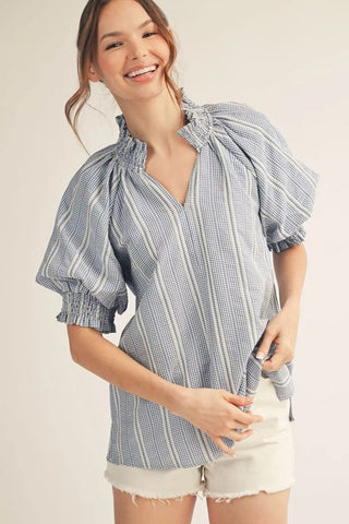 Woman wearing a blue and white checkered blouse with puff sleeves on a beige background