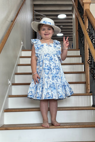 Child in a blue floral dress and hat standing on a staircase