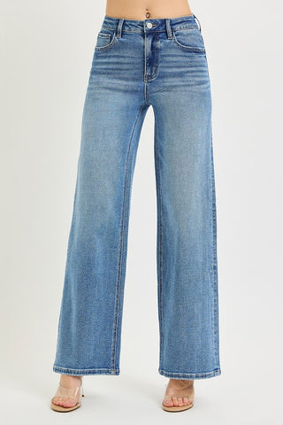 A person wearing high-waisted, wide-leg blue denim jeans with a light wash, paired with clear high-heeled sandals, shown against a plain light gray studio background.