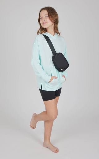 Person wearing a light blue hoodie and black shorts, carrying a black crossbody bag on a white background