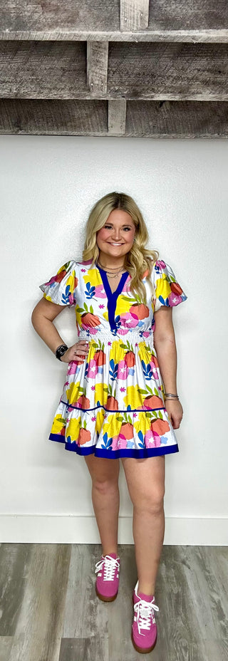 Woman wearing a colorful dress with fruit pattern against a wooden panel background
