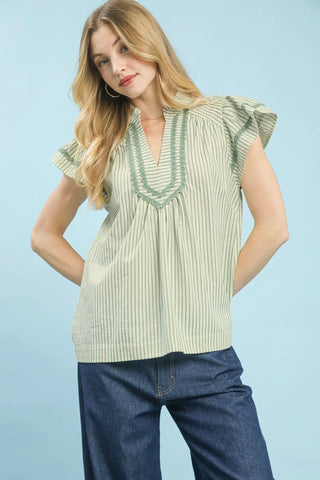 Woman wearing a green and white striped blouse with ruffled sleeves against a light blue background