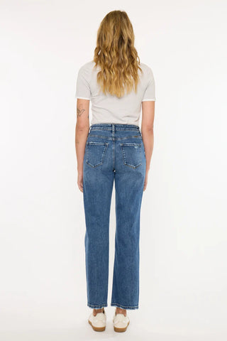A woman viewed from behind wearing blue straight-leg jeans, a white t-shirt, and white wedge sandals against a plain white studio background.