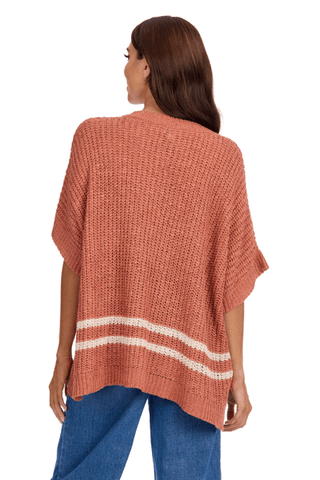 Woman wearing a rust-colored knit poncho with white stripes on a white background