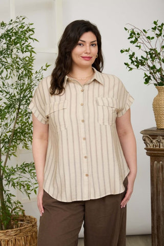 Woman wearing a beige striped shirt and brown pants standing in a room with plants.