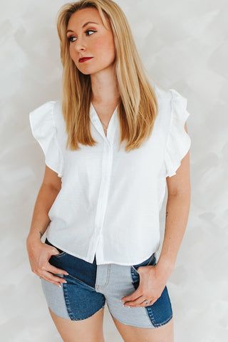 Woman wearing a white blouse with ruffled sleeves and denim shorts on a plain background