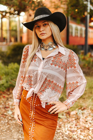 Woman wearing a patterned blouse and orange skirt with a black hat in an outdoor setting.