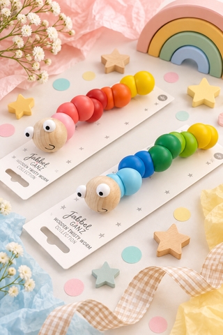 Two wooden caterpillar toys with colorful beads and googly eyes, displayed on branded white cards with decorative pastel props including stars, ribbons, flowers, and a rainbow.