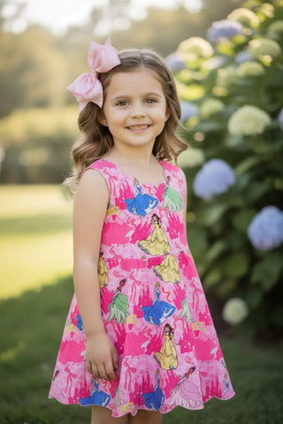 Young girl wearing a pink dress with princess prints, standing in a garden with flowers.