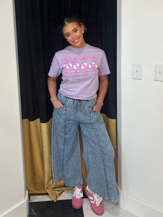 Person wearing a light purple t-shirt with text and graphics, blue jeans, and pink shoes in a room.