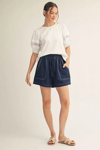 Woman wearing a white blouse and blue shorts on a plain background