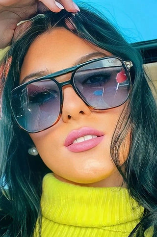 Person wearing sunglasses and a bright yellow top inside a vehicle.