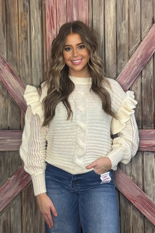 Woman wearing a cream sweater with ruffled sleeves against a wooden background
