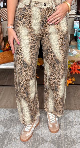 A person wearing leopard-print wide-leg pants with beige sneakers, shown from the waist down in a retail setting.