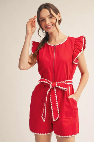 Woman wearing a red romper with white trim on a beige background