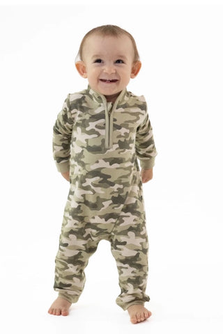 A baby standing and smiling while wearing a long-sleeve camouflage footed sleeper with a half-zip neckline, photographed against a plain white background.