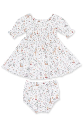 A baby girl's two-piece outfit set consisting of a smocked dress and matching bloomers, both in white cotton fabric with a delicate, all-over woodland print of deer, flowers, and leaves in muted earthy tones.