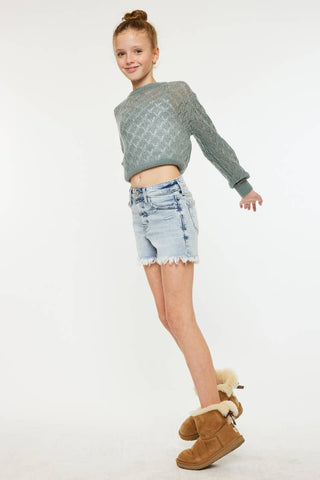 Young girl wearing a gray sweater, denim shorts, and brown boots on a white background