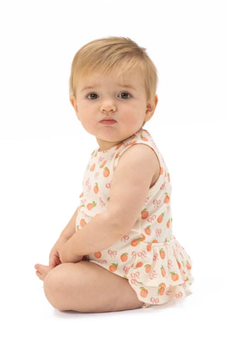 Baby sitting on a white background wearing a sleeveless romper with fruit pattern