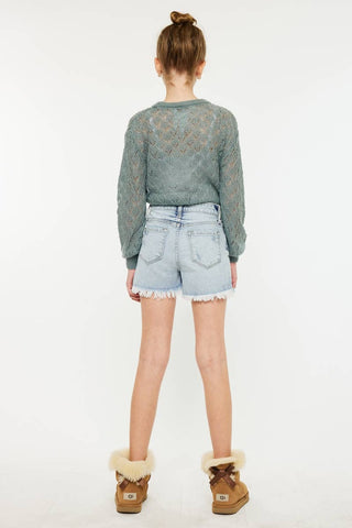 Person wearing a green sweater with lace details, light blue denim shorts, and brown boots on a white background