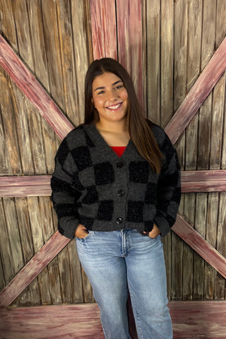 Person wearing a black coat and jeans standing on a wooden floor.