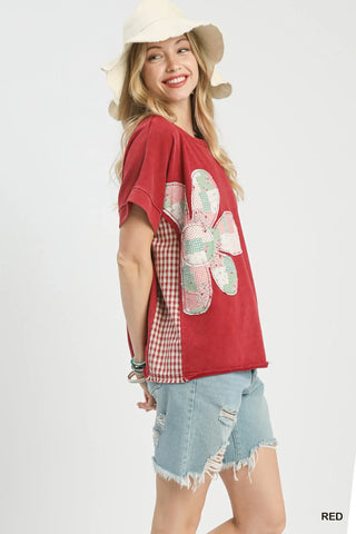 Woman wearing a red shirt with a large flower design and denim shorts on a white background