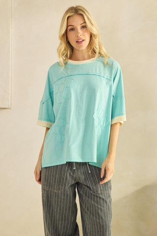 Woman wearing a light blue top and striped pants against a beige wall.