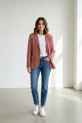 Woman wearing a red plaid blazer, white shirt, blue jeans, and white sneakers in a minimalistic room.