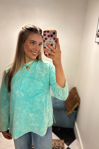 Woman taking a mirror selfie wearing a light blue top in a room with a couch and decorative items.