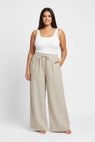 Woman wearing a white tank top and beige wide-leg pants on a white background
