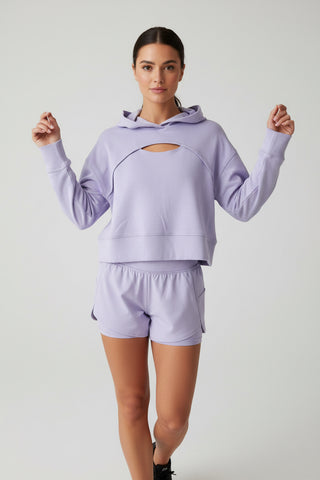 Woman wearing a light purple hoodie and shorts on a plain background