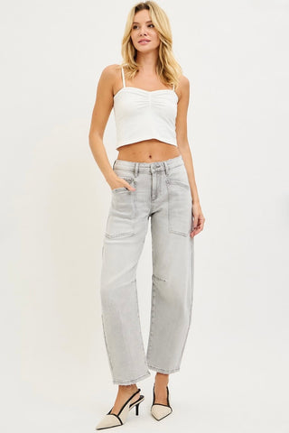 A woman modeling light-wash wide-leg cropped jeans with a white ruched spaghetti-strap crop top and pointed-toe heels against a plain white studio background.