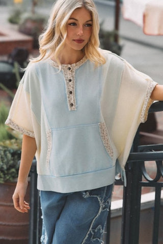 Woman wearing a light blue and beige top with lace details outdoors.