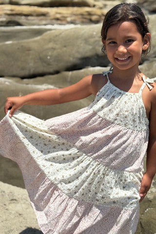 Young girl in a floral dress standing on a rocky beach.