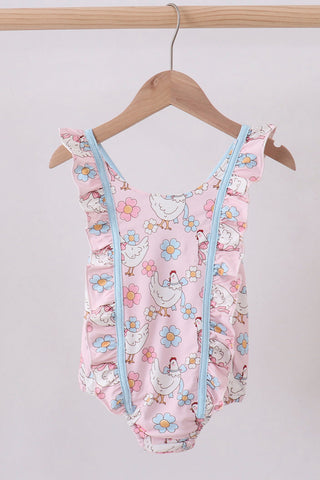 Pink children's swimsuit with chicken and flower pattern on a wooden hanger against a white background