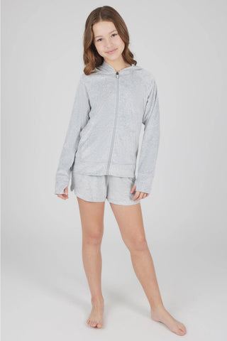 A young girl modeling a light gray heathered zip-up hoodie and matching shorts set against a plain light gray studio background.