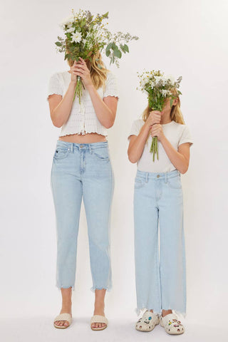 Two people wearing white tops and light blue jeans holding flower bouquets against a white background