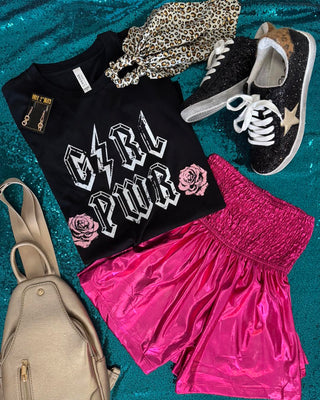 Black t-shirt with 'Girl Power' text, pink shorts, black sneakers, and beige backpack on a blue glittery surface.