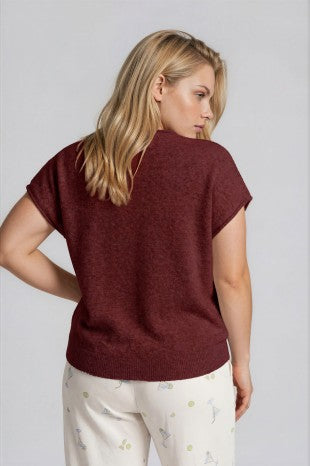 Woman wearing a burgundy sweater and white pants with a subtle pattern on a plain background