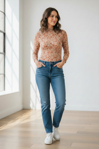 Woman wearing a floral top and blue jeans standing in a well-lit room.