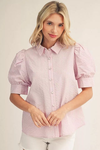 Woman wearing a pink checkered blouse with puff sleeves on a plain background