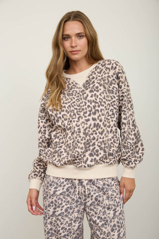 A woman modeling a matching two-piece loungewear set featuring a beige and gray leopard print pattern with solid cream ribbed trim, including a long-sleeve top and sweatpants, against a plain light gray studio background.